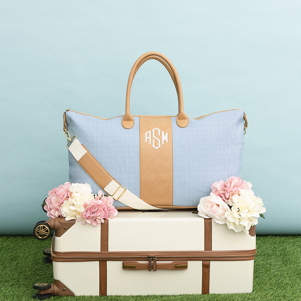 navy seersucker weekender and vintage suitcase on grass and blue