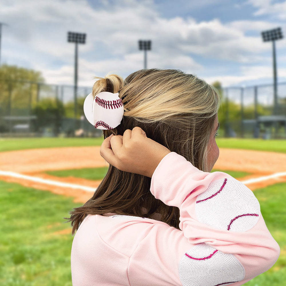 Person wearing a pink sweatshirt with baseball design hair clip on a baseball field