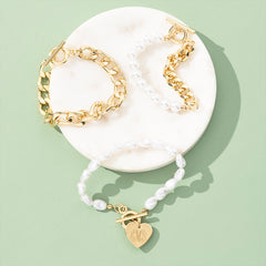 Set of gold and pearl bracelets with a heart-shaped charm on a white dish against a light green background