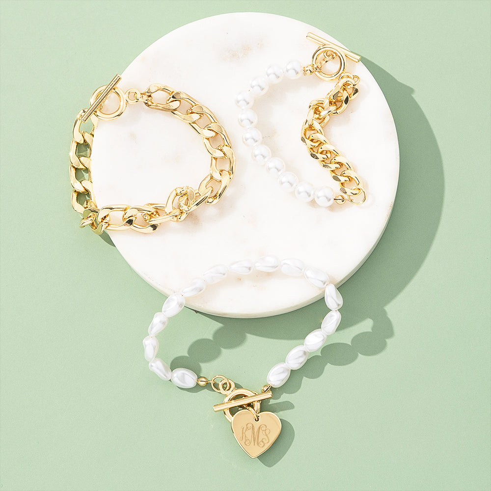 Set of gold and pearl bracelets with a heart-shaped charm on a white dish against a light green background