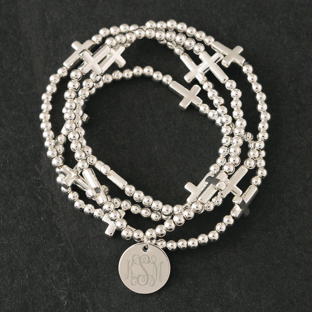 close up of monogrammed silver cross bracelet stack