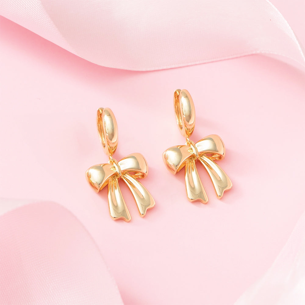 bow huggie hoop earrings on pink background