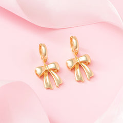 bow huggie hoop earrings on pink background