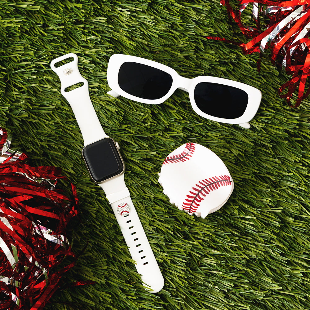 White smartwatch, sunglasses, baseball hair clip, and red pom-poms on green grass