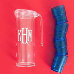 Clear pitcher with 'KHM' monogram and blue acrylic cups on a red background