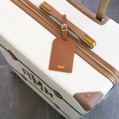 Suitcase with brown handle and luggage tag featuring 'KLM' on a textured surface.