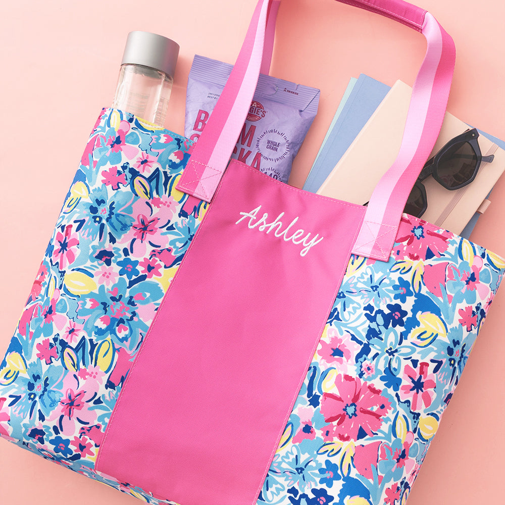 Pink tote bag with floral sides, filled with items on a pink background
