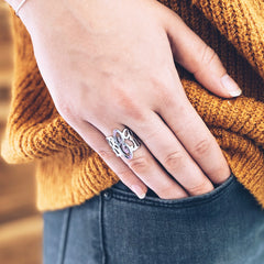A close-up of a person's hand wearing a silver ring, resting on their hip over a mustard yellow knit sweater and dark gray jeans.