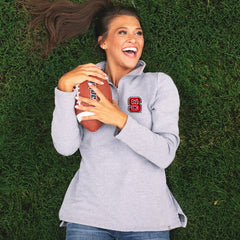 girl laying in grass wearing nc state pullover sweatshirt and holding football