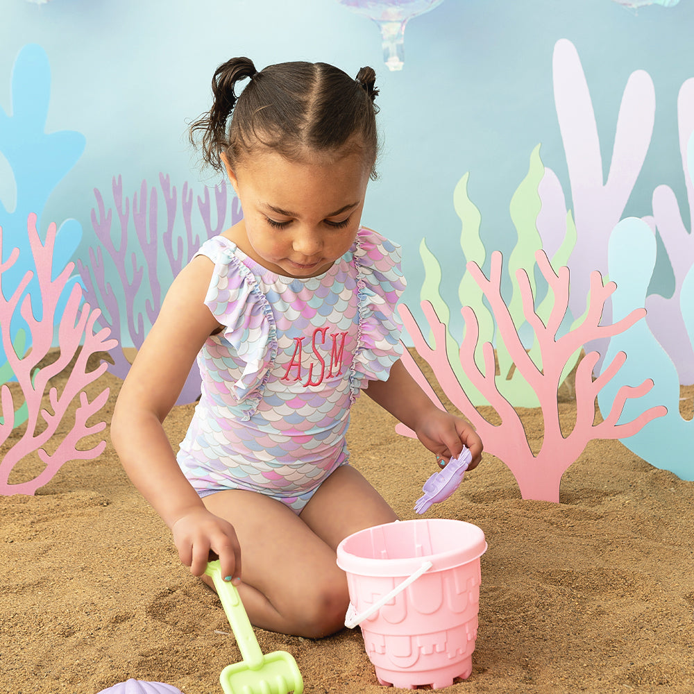 girl wearing ruffle swimsuit in mermaid playing in sand