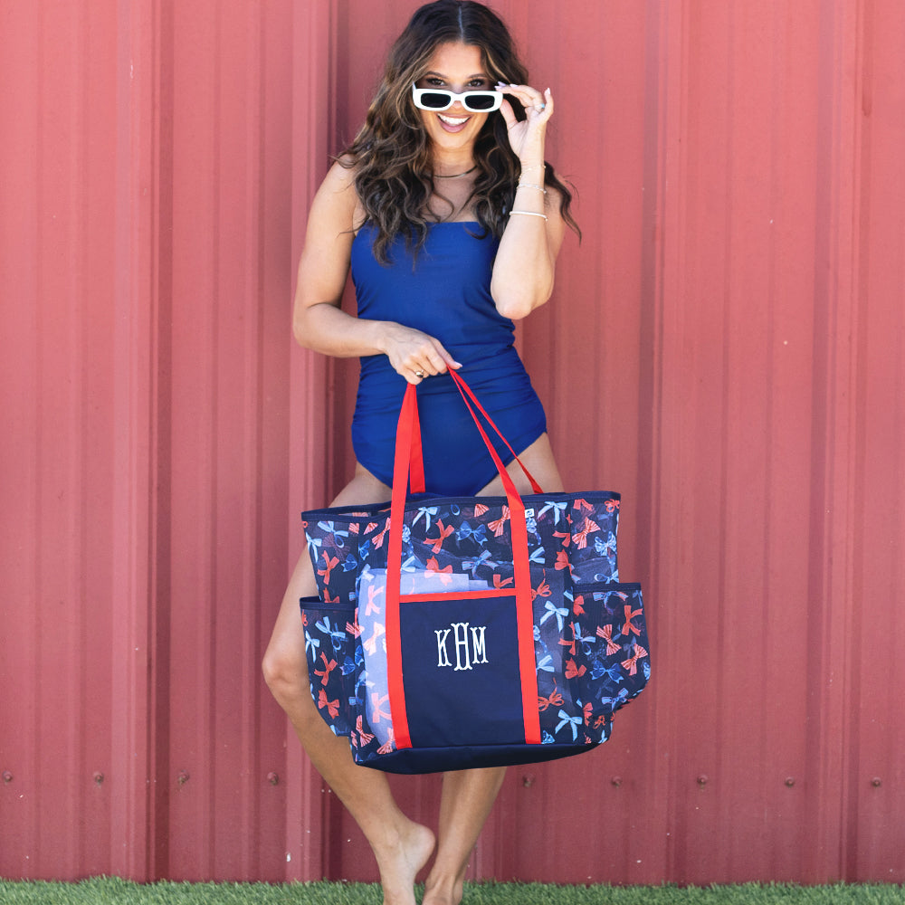 woman holding america bow print mesh tote wearing a one piece swimsuit and sunglasses