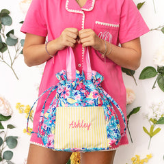 Person holding a colorful toiletry bag with 'Ashley' embroidered on it, wearing a pink outfit.