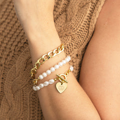Gold chain bracelet, pearl beaded bracelet, and ivory bracelet on a wrist with a textured brown background