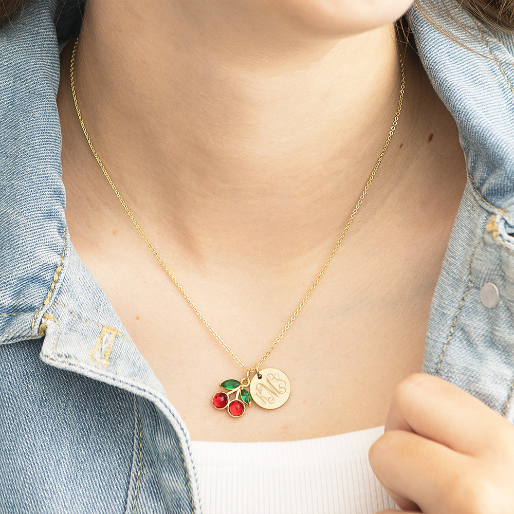 Gold necklace with cherry pendants on a person wearing a denim jacket.