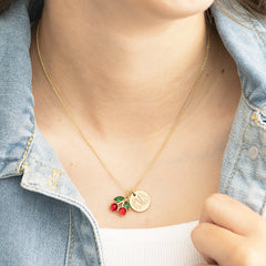 Gold necklace with cherry pendants on a person wearing a denim jacket.