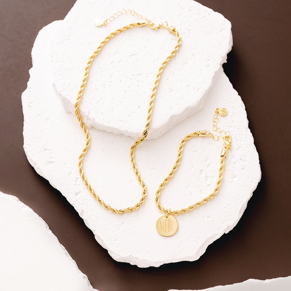 Gold necklace and bracelet on a textured white surface with a brown background