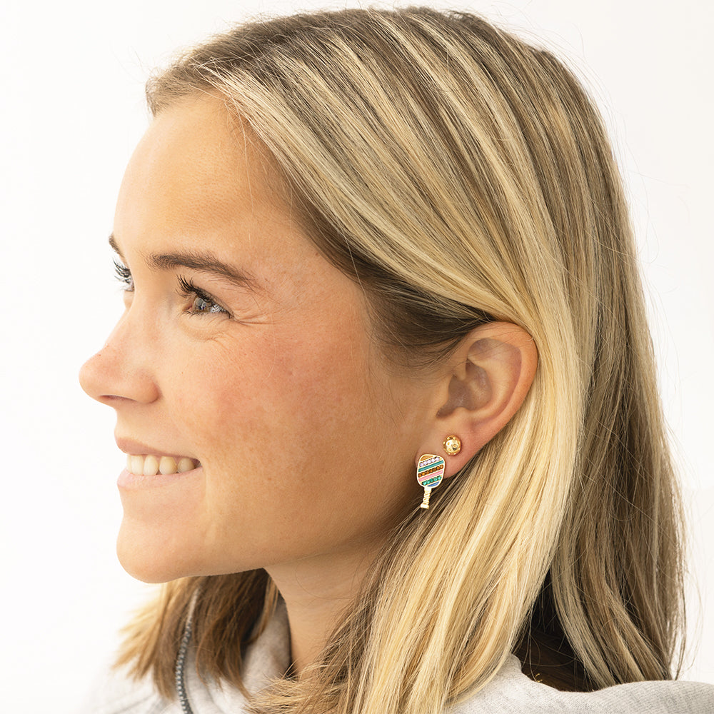Close-up of a woman wearing colorful pickleball paddle earrings on a white background