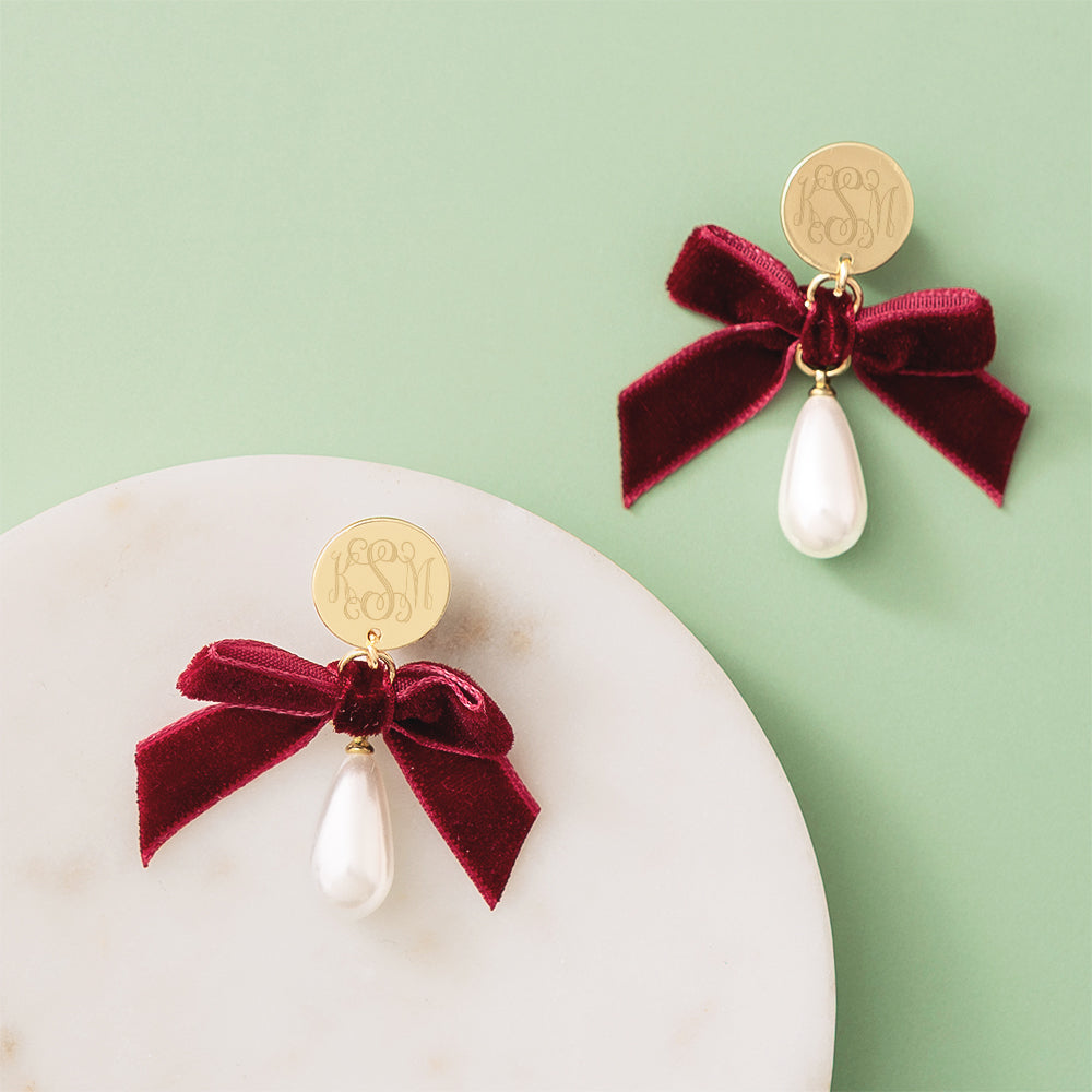 Monogrammed velvet bow earrings on green background