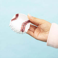 Hand holding a small white and red baseball hair clip against a light blue background