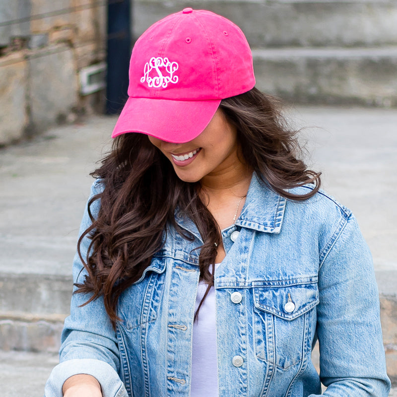 Woman wearing a pink cap with a monogram and a denim jacket outdoors.