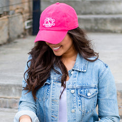 Woman wearing a pink cap with a monogram and a denim jacket outdoors.