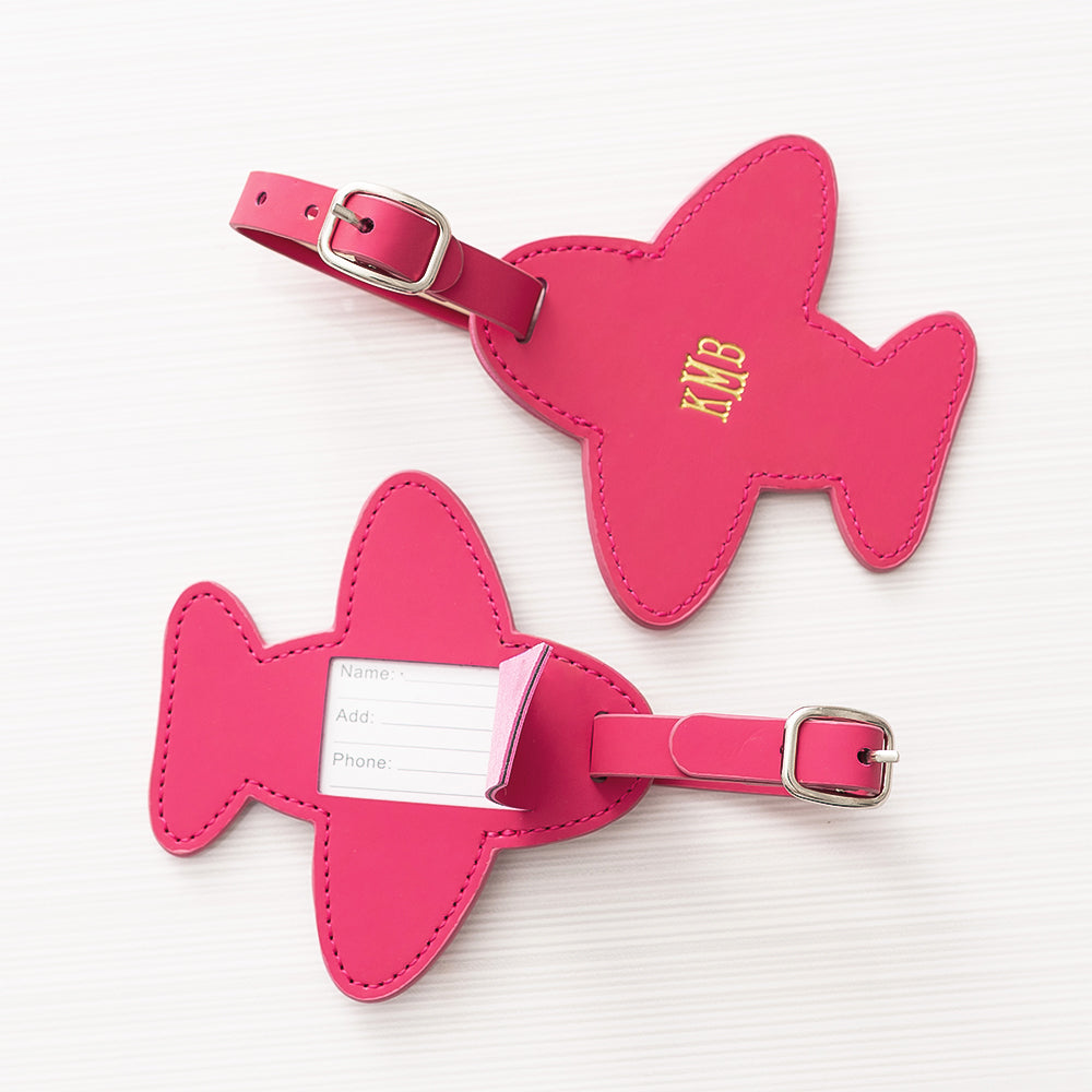 Two pink airplane-shaped luggage tags with silver buckles on a white background