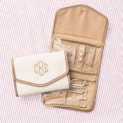 Inside of jewelry organizer with jewelry in multiple zipper compartments on a pink striped background