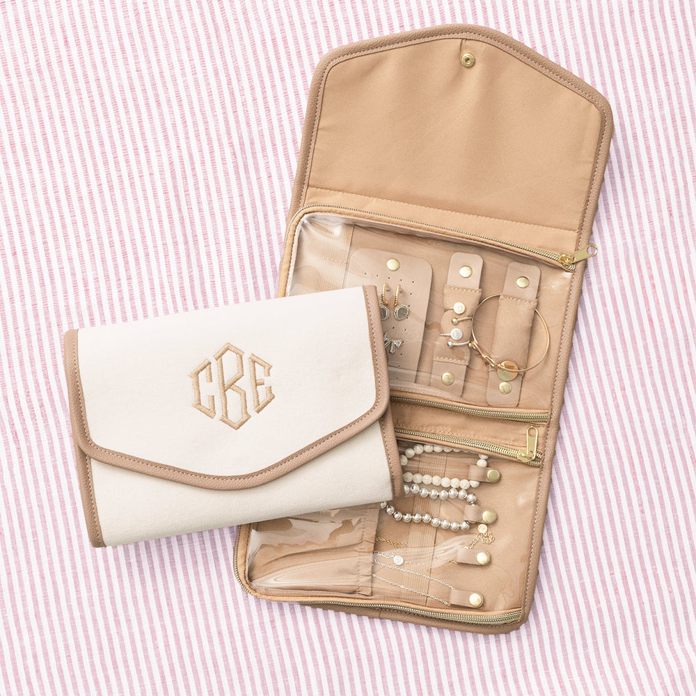 Inside of jewelry organizer with jewelry in multiple zipper compartments on a pink striped background