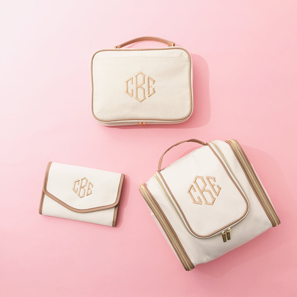 Set of ivory-colored bags with tan monogram on a pink background
