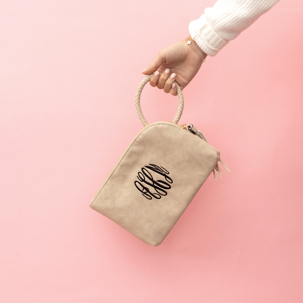 taupe monogrammed wristlet clutch in front of pink paper