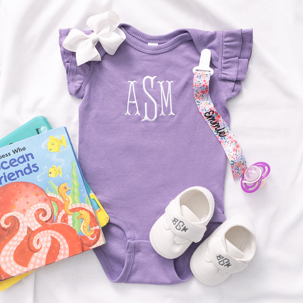Girls purple monogrammed one piece with white shoes and floral paci clip.