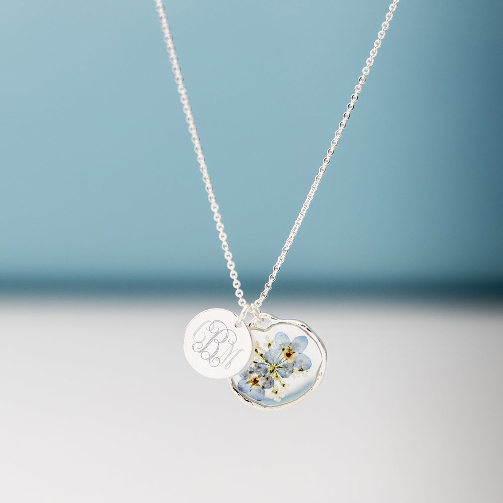 silver forget me not necklace hanging in front of blue paper
