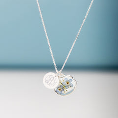 silver forget me not necklace hanging in front of blue paper