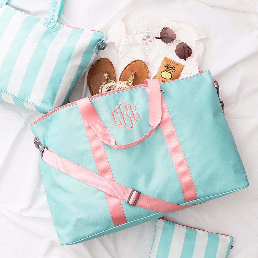 Mint bag with pink straps on a white surface, surrounded by striped items and sunglasses.