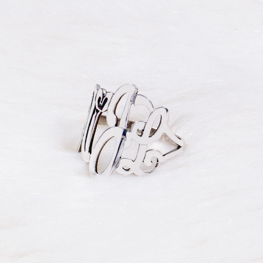 A silver ring featuring monogram in cursive script, resting on a white textured surface.