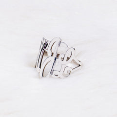 A silver ring featuring monogram in cursive script, resting on a white textured surface.