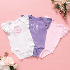 Three baby bodysuits with monogrammed letters on a pink background with flowers.