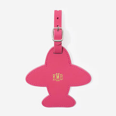 Pink airplane-shaped leather luggage tag with gold monogram on a white background