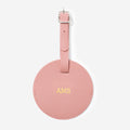 Pink leather luggage tag with gold monogram on a white background