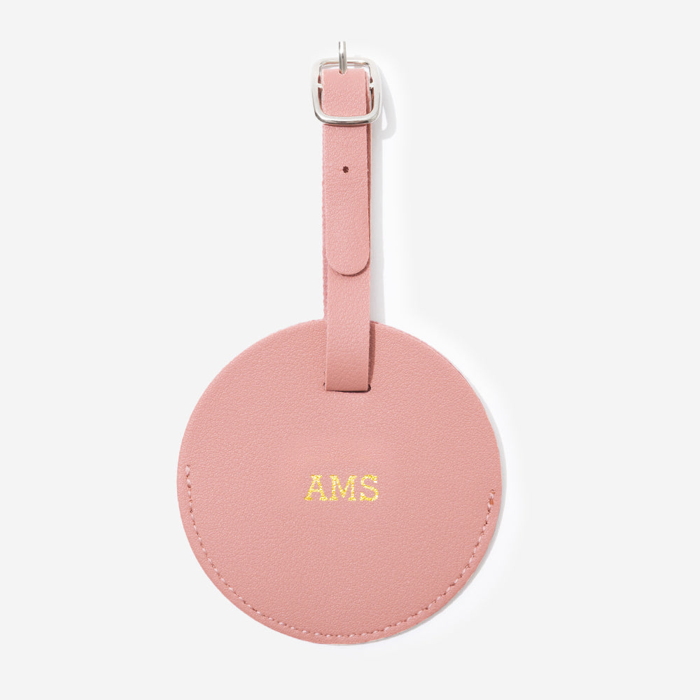 Pink leather luggage tag with gold monogram on a white background