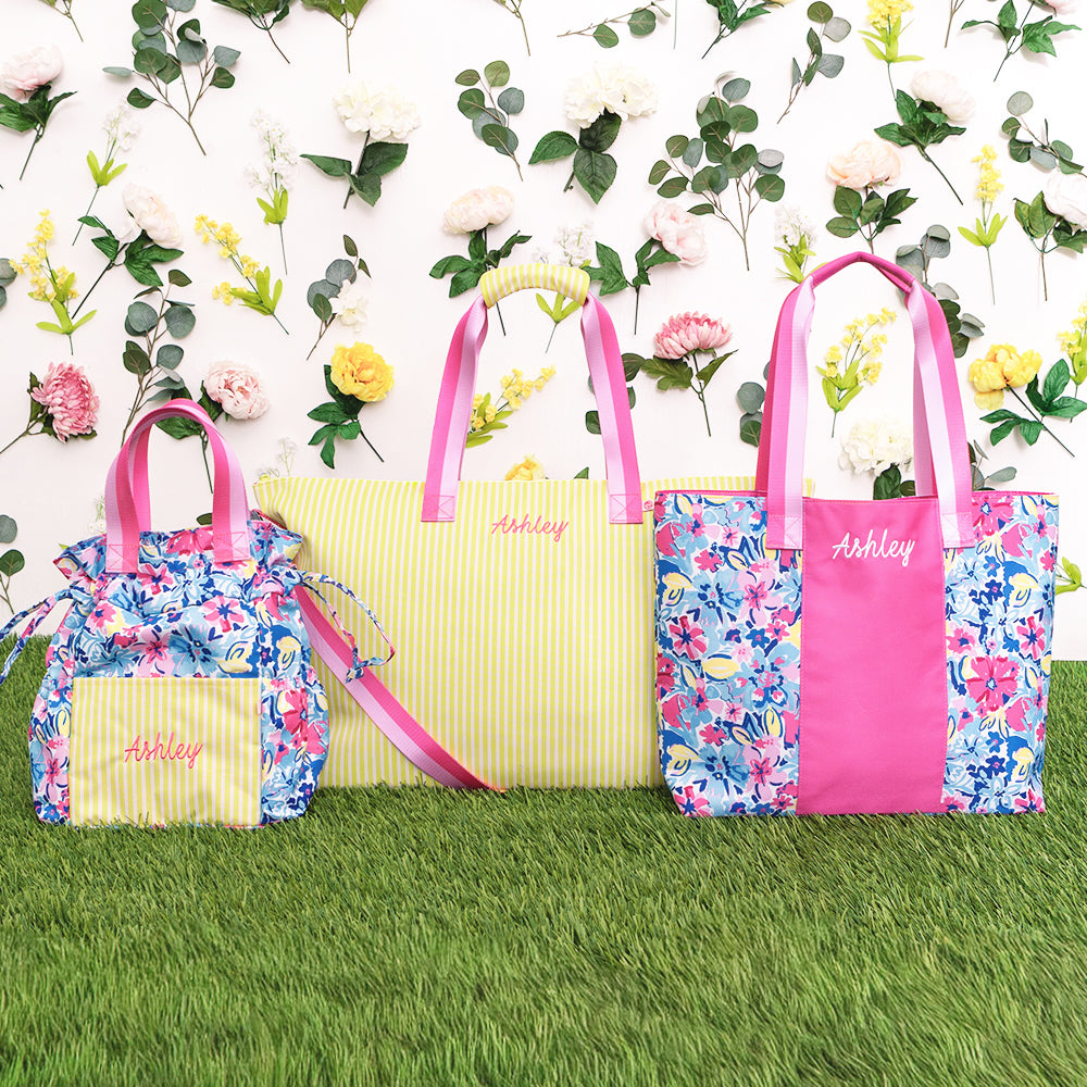 Three bags with floral patterns and pink accents on a grassy background with flowers.