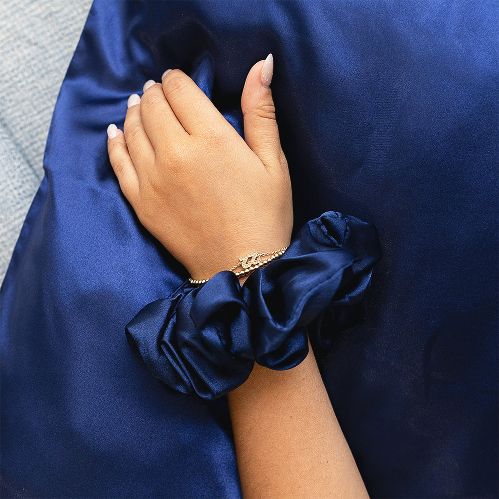 Hand wearing a blue scrunchie on wrist on a blue satin fabric