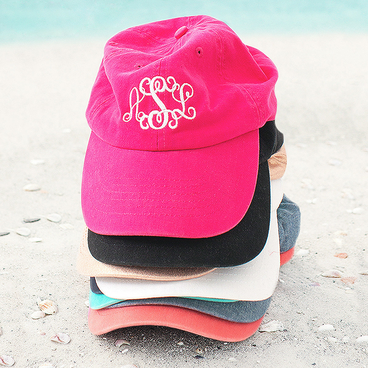 stacked monogrammed baseball hats on the beach
