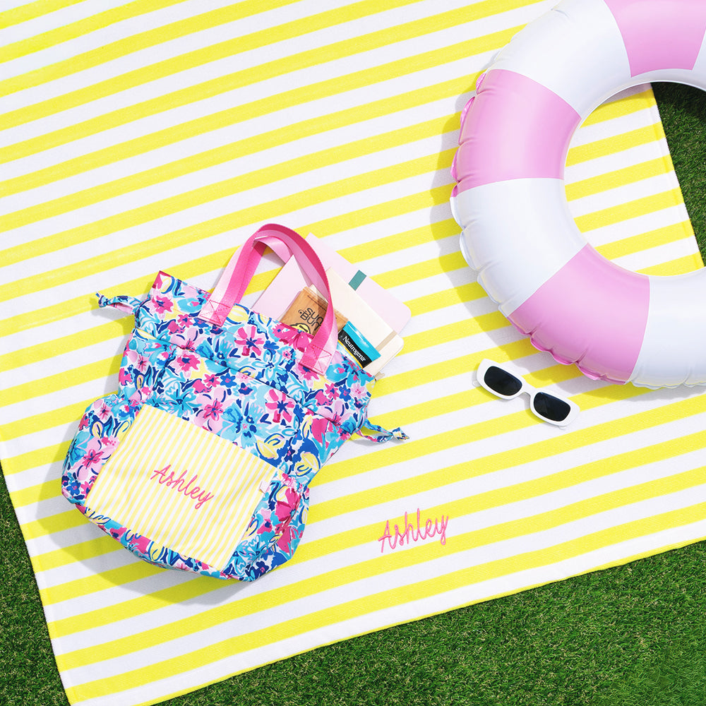 yellow striped beach towel with floral toiletry bag and pool float.