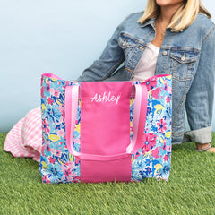 Floral tote bag with pink center stripe and 'Ashley' embroidery, held by a person on grass.