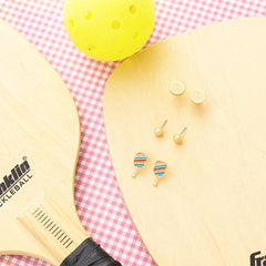 Yellow paddle and pickleball with earrings on a checkered background