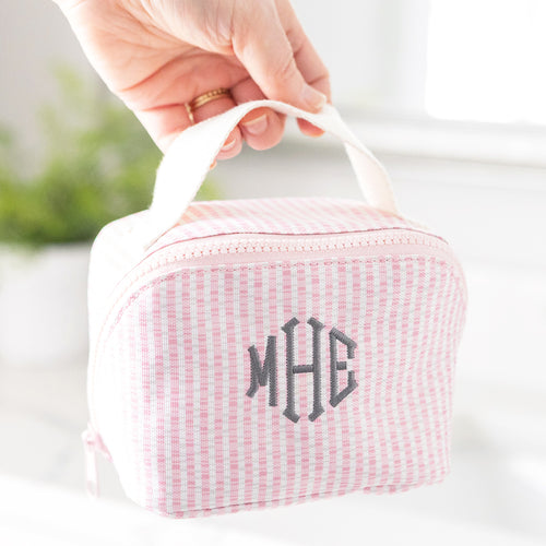 Pink seersucker pouch with initials 'MHE' held by a hand against a blurred background