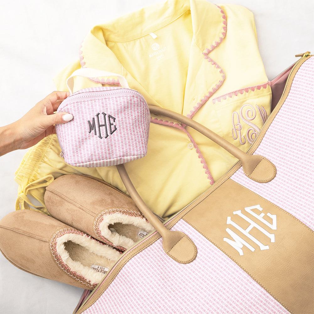 Pink makeup bag with monogram, yellow jacket, and tan slippers on a white background
