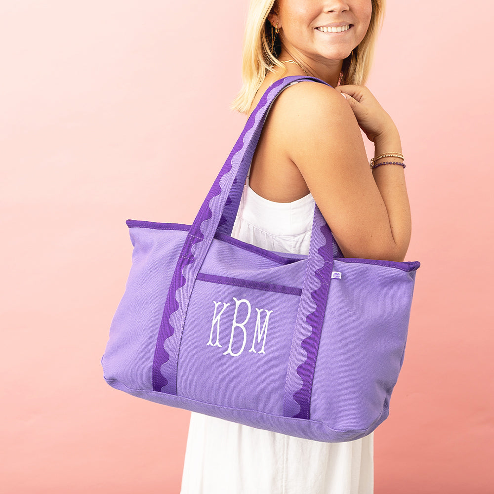 Woman carrying a purple tote bag with initials 'KBM' on a pink background