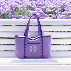 Purple tote bag with initials 'KBM' on a white bench in front of lavender flowers